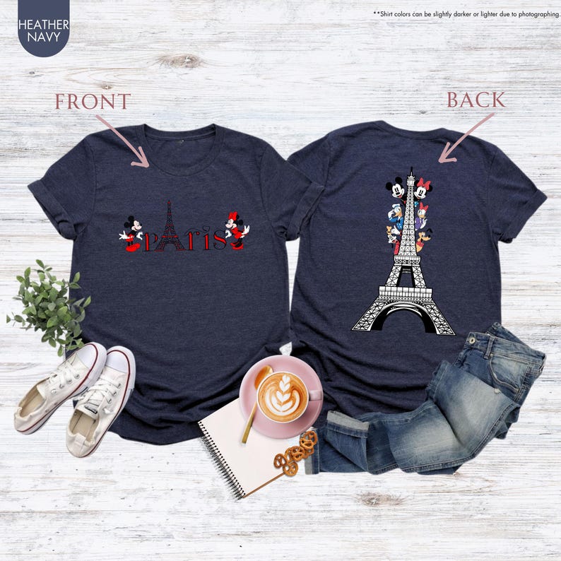 Pu&ograve; includere: T-shirt blu navy con grafica della Torre Eiffel e la scritta "Paris" in rosso, con Topolino e Minnie. Il retro della maglietta presenta la Torre Eiffel con personaggi Disney. La maglietta &egrave; esposta con jeans e scarpe.
