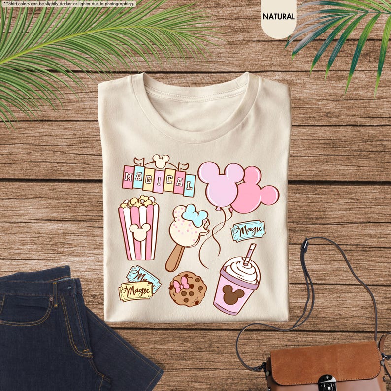 Puede incluir: Una camiseta beige con un dise&ntilde;o caprichoso que presenta orejas de Mickey Mouse, palomitas de ma&iacute;z, un helado de Mickey Mouse, un batido de Mickey Mouse y boletos que dicen "Magic".