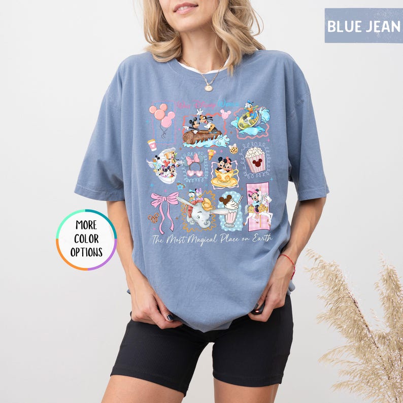 May include: Blue jean colored t-shirt with a graphic featuring various cartoon characters and the text "The Most Magical Place on Earth." The shirt has short sleeves and a crew neck. A button on the left side says "More Color Options."