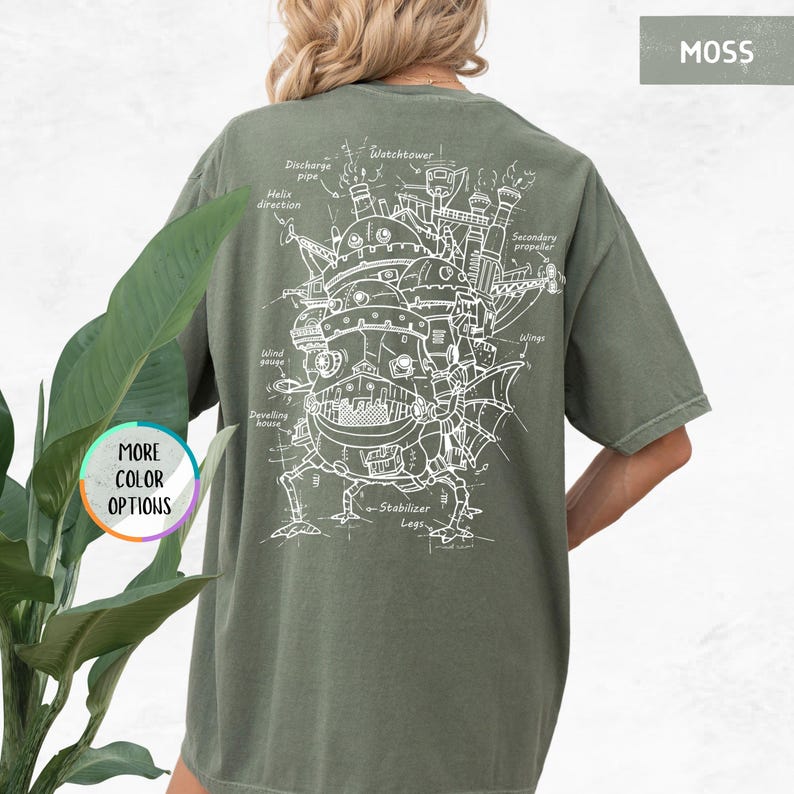 Op de afbeelding: Mosgroen t-shirt met een witte schematische tekening van een fantastische bewegende structuur. Het ontwerp bevat labels zoals "Watchtower" en "Wings". Het shirt heeft ook de tekst "MORE COLOR OPTIONS" linksonder.