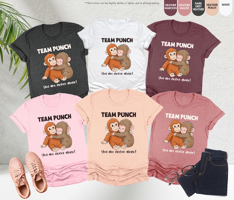 Puede incluir: Una colecci&oacute;n de camisetas en varios colores, incluyendo gris jaspeado, blanco y rosa. Cada camiseta presenta el texto "TEAM PUNCH" sobre una ilustraci&oacute;n de dos monos abraz&aacute;ndose, con la frase "You are never alone!" debajo.