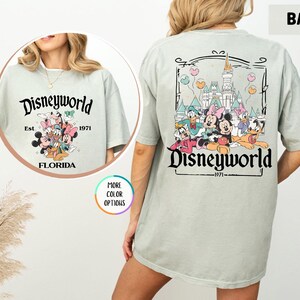 Puede incluir: Camiseta verde claro con el texto "Disneyworld" y el a&ntilde;o "1971". La parte delantera de la camiseta tiene un gr&aacute;fico de Mickey y Minnie Mouse, Donald y Daisy Duck y Goofy. La parte trasera de la camiseta tiene el castillo de Cenicienta y los mismos personajes.