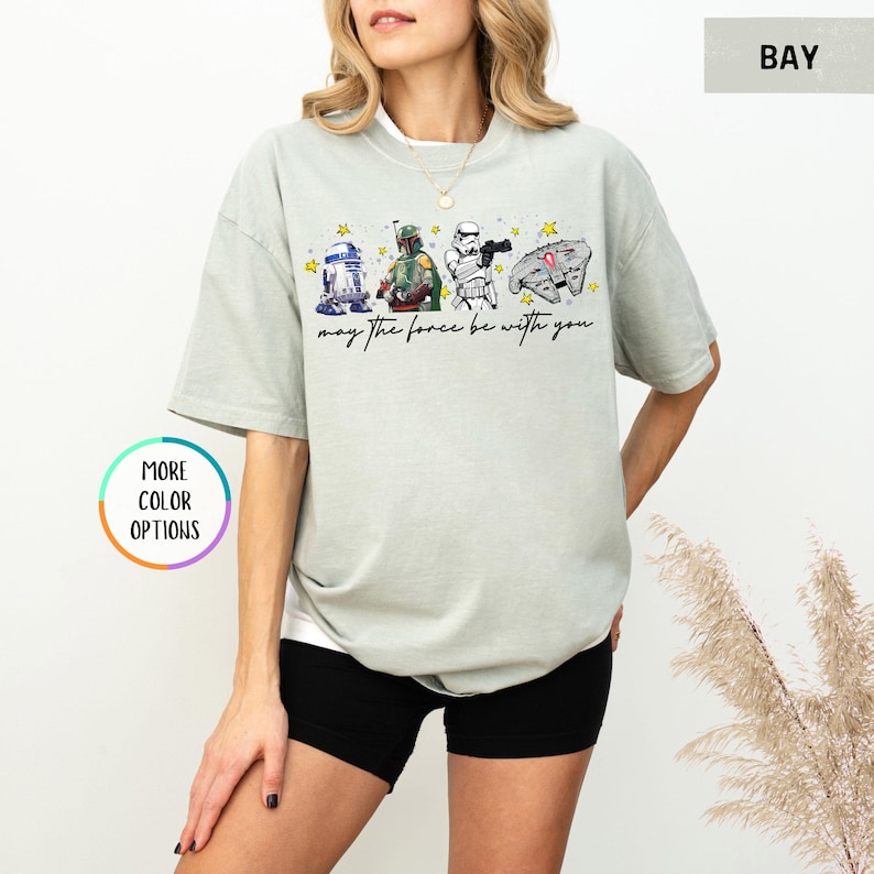 Puede incluir: Camiseta verde claro con personajes de Star Wars: R2-D2, Boba Fett, un Stormtrooper y una nave espacial. La frase "may the force be with you" est&aacute; impresa debajo. La camiseta es de corte holgado.