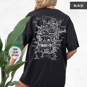 Op de afbeelding: Zwart t-shirt met een witte technische tekening van een fantasiegebouw, met opschriften als "Watchtower" en "Stabilizer Legs". Het shirt heeft ook de tekst "BLACK" en "MORE COLOR OPTIONS".