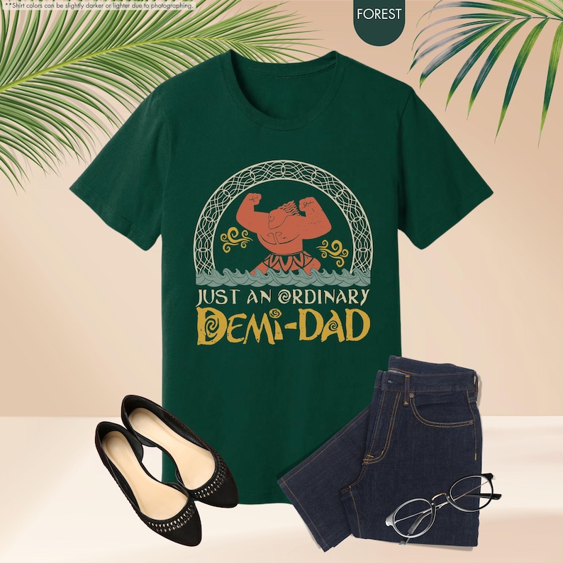 Puede incluir: Camiseta verde con una imagen de dibujos animados de un hombre musculoso con cuerpo rojo y pelo amarillo. El texto "Just an ordinary Demi-Dad" est&aacute; impreso en amarillo en la camiseta.