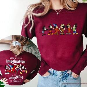 Puede incluir: Sudadera granate con una fila de personajes de dibujos animados en el pecho. La parte posterior de la sudadera muestra el texto "WITH A LITTLE Imagination Anything IS POSSIBLE" con personajes de dibujos animados.