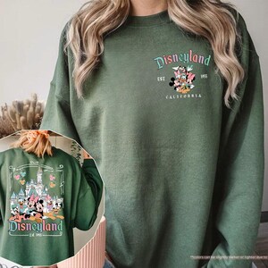 May include: A green sweatshirt with a Disneyland logo featuring Mickey Mouse and friends. The logo says "Disneyland Est. 1955 California".