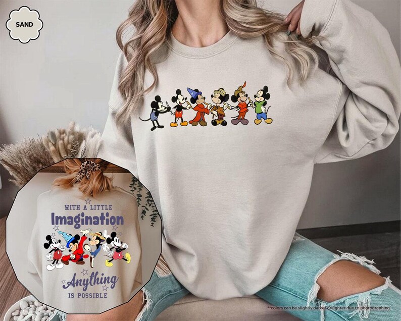 Puede incluir: Sudadera color arena con una fila de personajes de dibujos animados de Mickey Mouse. La sudadera tiene cuello redondo y mangas largas. Una imagen m&aacute;s peque&ntilde;a muestra el texto "With a Little Imagination Anything is Possible" con personajes de Mickey Mouse.