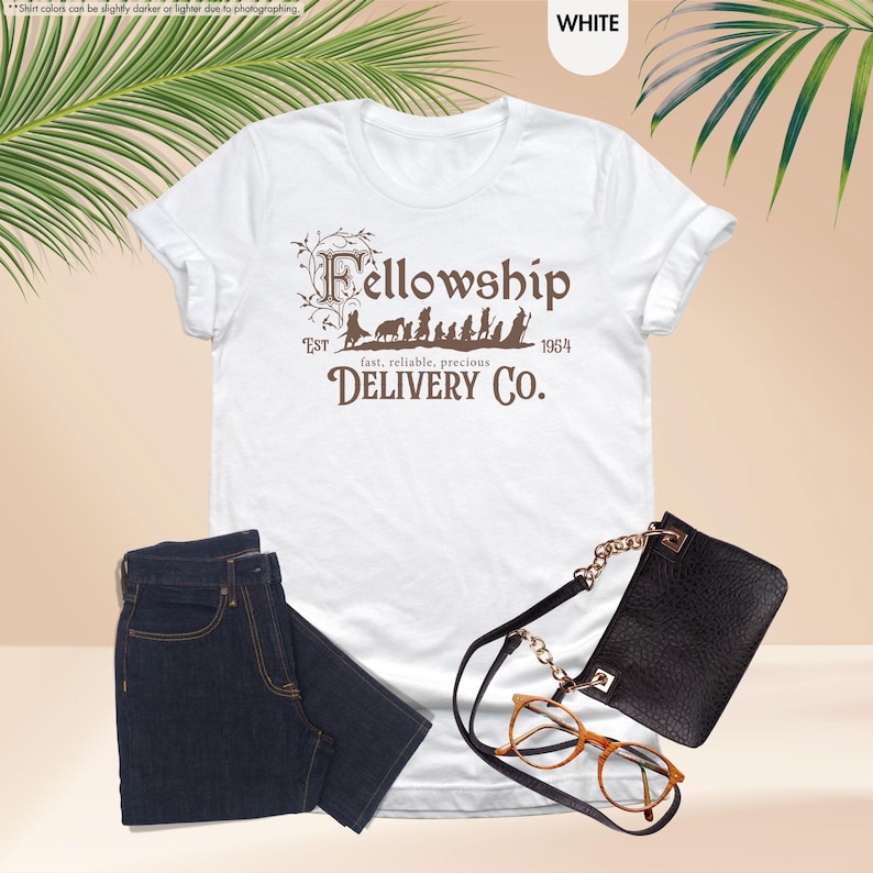 Puede incluir: Camiseta blanca con un gr&aacute;fico marr&oacute;n de los personajes de la Comunidad del Anillo caminando con el texto "Fellowship Est 1954 fast, reliable, precious DELIVERY CO."