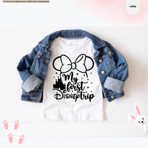 Pu&ograve; includere: Maglietta bianca con una grafica nera di orecchie di Topolino con un fiocco, un castello e il testo "My first DISNEptrip".
