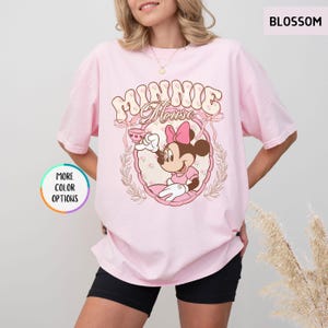May include: Pink t-shirt with a vintage-style graphic of Minnie Mouse holding a teacup. The graphic features the text "Minnie Mouse" in a floral design.