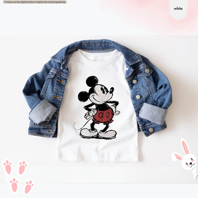 May include: A white t-shirt featuring a black and red graphic of Mickey Mouse, paired with a denim jacket. The cartoon character is depicted with a classic pose. The outfit is styled on a white background.
