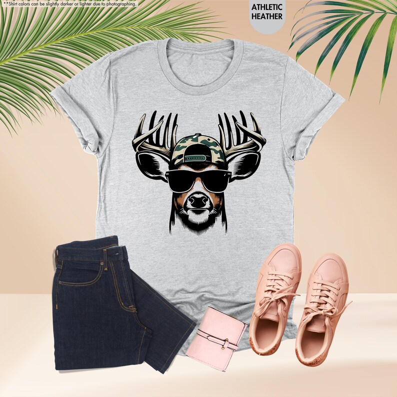 May include: A gray t-shirt with a graphic of a deer wearing sunglasses and a camouflage baseball cap. The deer has large antlers. The text "ATHLETIC HEATHER" is printed on the shirt.