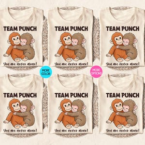 Puede incluir: Camisetas color crema con una ilustraci&oacute;n de dibujos animados de dos monos abraz&aacute;ndose. El texto "TEAM PUNCH" est&aacute; encima de la imagen, y "You are never alone!" debajo. Tambi&eacute;n se muestran opciones de color y variaciones.