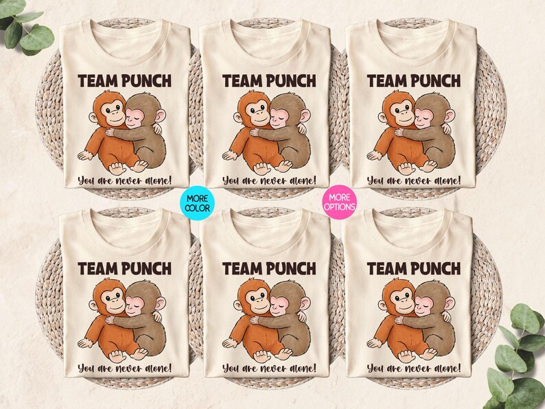 Puede incluir: Camisetas color crema con una ilustraci&oacute;n de dibujos animados de dos monos abraz&aacute;ndose. El texto "TEAM PUNCH" est&aacute; encima de la imagen, y "You are never alone!" debajo. Tambi&eacute;n se muestran opciones de color y variaciones.