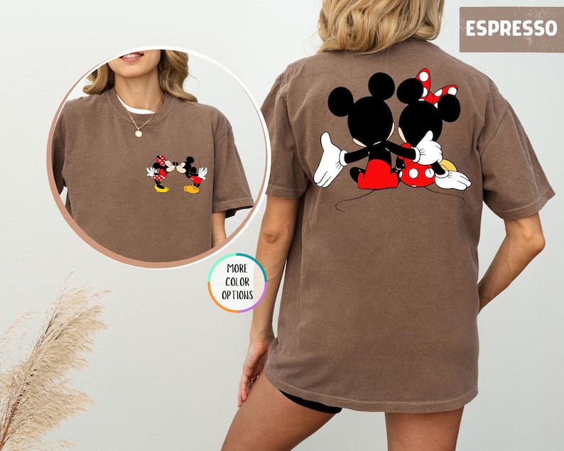 May include: Espresso-coloured t-shirt featuring Mickey and Minnie Mouse. The front of the shirt shows the characters kissing, while the back displays them embracing. The shirt has a classic, relaxed fit and is a comfortable choice for casual wear.