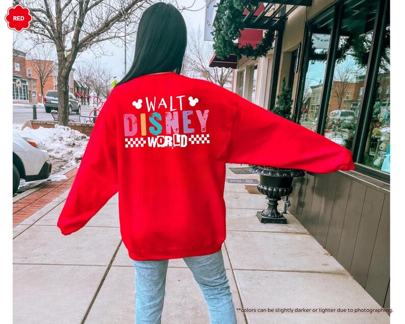 Puede incluir: Una sudadera roja brillante con las palabras "WALT DISNEY WORLD" en letras de bloque coloridas. El texto est&aacute; en la parte posterior de la sudadera. La sudadera tiene mangas largas y cuello redondo.