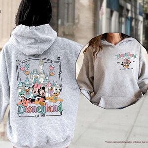 May include: A gray hooded sweatshirt with a graphic print of Mickey Mouse and friends in front of the Disneyland castle. The text "Disneyland Est. 1955" is printed below the graphic.