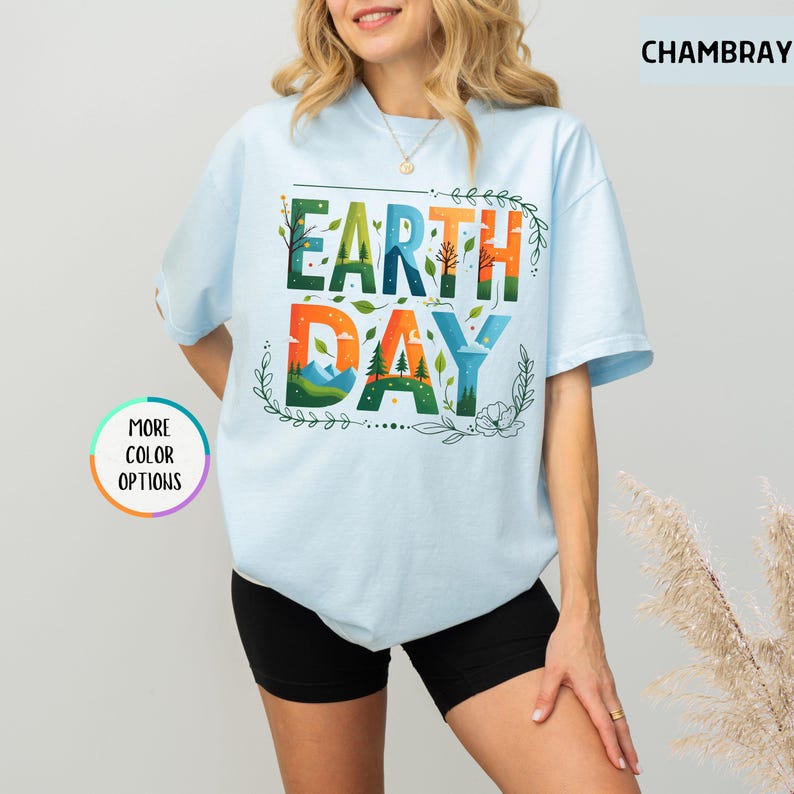 May include: A light blue t-shirt with the text "Earth Day" in colorful letters with a nature-inspired design. The letters are surrounded by green leaves and flowers.