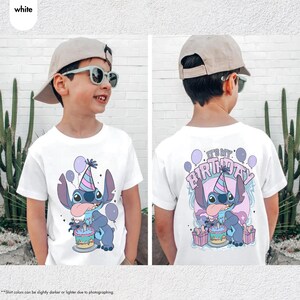 May include: White t-shirt with a cartoon character design, wearing a party hat and holding a cake, with balloons. The back of the shirt says "IT'S MY BIRTHDAY!" in a playful font. The design uses blue, purple, and pink colours.