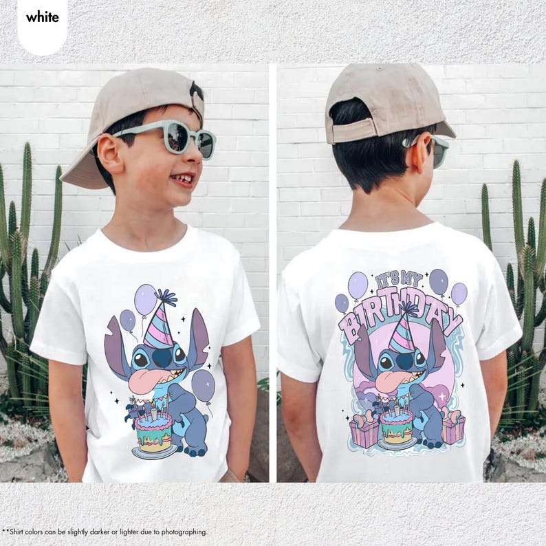 May include: White t-shirt with a cartoon character design, wearing a party hat and holding a cake, with balloons. The back of the shirt says "IT'S MY BIRTHDAY!" in a playful font. The design uses blue, purple, and pink colours.