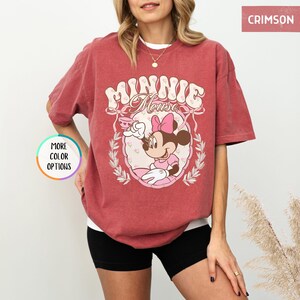 May include: A red t-shirt with a vintage-style graphic of Minnie Mouse holding a teacup. The graphic features the text "Minnie Mouse" in a retro font.