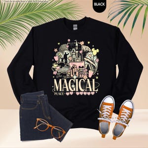 Pode incluir: Camisola preta de manga comprida com um design gr&aacute;fico colorido com um castelo, Mickey Mouse e o texto "The Most Magical Place". A camisola &eacute; combinada com jeans azuis, &oacute;culos laranja e t&eacute;nis laranja.