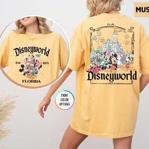 Puede incluir: Camiseta color mostaza con el texto "Disneyworld" y un gr&aacute;fico de personajes de Disney. La parte delantera muestra "Disneyworld Est. 1971 Florida" con personajes de Disney. La parte trasera tiene un gr&aacute;fico m&aacute;s grande de personajes de Disney y "Disneyworld 1971".
