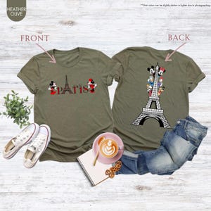 Pu&ograve; includere: T-shirt verde oliva melange con grafica della Torre Eiffel e personaggi dei cartoni animati. La parte anteriore della maglietta dice "Parigi" con Topolino e Minnie. Il retro della maglietta presenta la Torre Eiffel con personaggi dei cartoni animati.