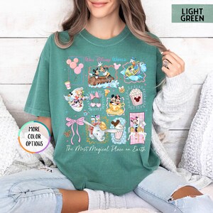 May include: Light green t-shirt with a colorful Disney World graphic. The graphic includes various Disney characters and icons, such as Mickey and Minnie Mouse, Dumbo, and popcorn. The text "Our Disney World" and "The Most Magical Place on Earth" are also featured.
