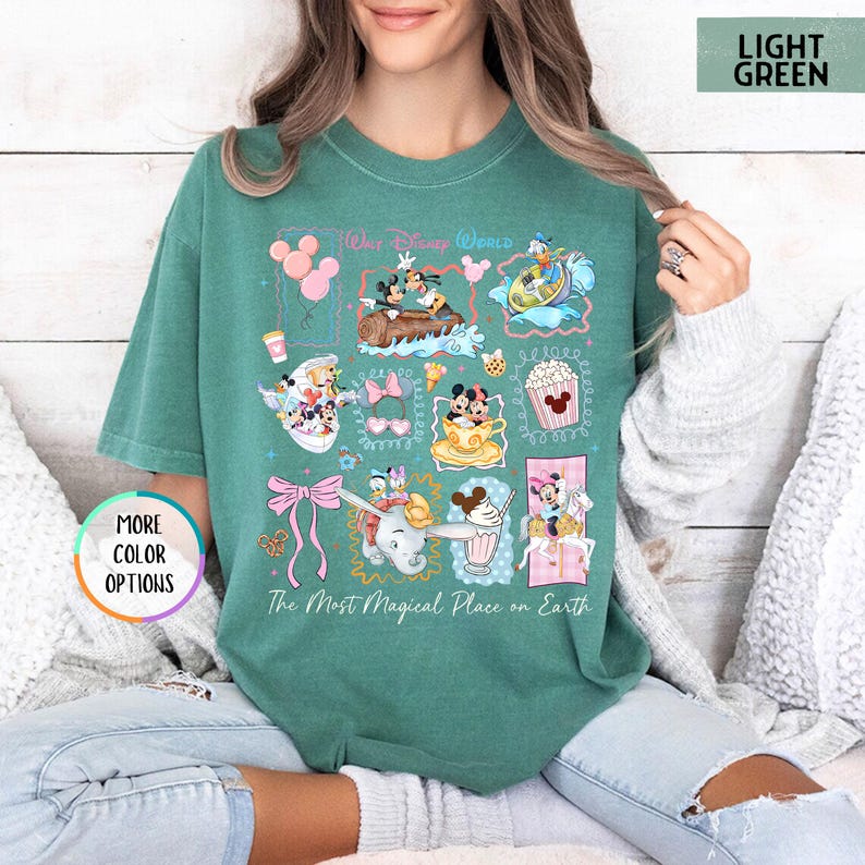 May include: Light green t-shirt with a colorful Disney World graphic. The graphic includes various Disney characters and icons, such as Mickey and Minnie Mouse, Dumbo, and popcorn. The text "Our Disney World" and "The Most Magical Place on Earth" are also featured.