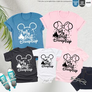 Pode incluir: Quatro camisetas com o texto "My first DISNEptrip" em letras brancas e pretas. As camisetas apresentam uma cabe&ccedil;a do Mickey Mouse, uma cabe&ccedil;a da Minnie Mouse e uma silhueta do castelo da Cinderela. As camisetas s&atilde;o de v&aacute;rias cores, incluindo azul, rosa, branco e cinza.