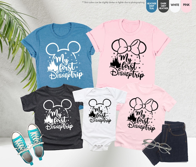 Pode incluir: Quatro camisetas com o texto "My first DISNEptrip" em letras brancas e pretas. As camisetas apresentam uma cabe&ccedil;a do Mickey Mouse, uma cabe&ccedil;a da Minnie Mouse e uma silhueta do castelo da Cinderela. As camisetas s&atilde;o de v&aacute;rias cores, incluindo azul, rosa, branco e cinza.