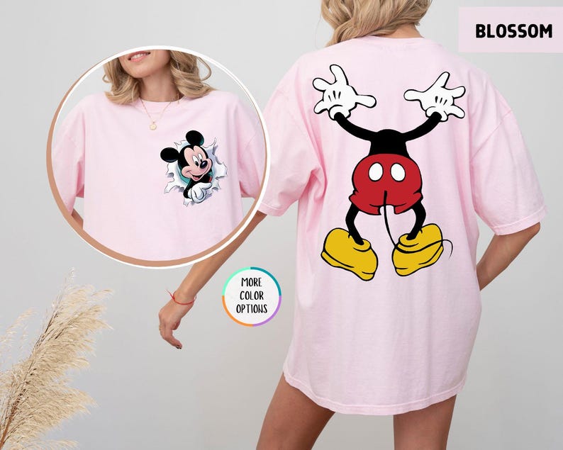 May include: A pale pink t-shirt with a Mickey Mouse design. The front has Mickey breaking through a hole, and the back shows a full cartoon image of Mickey Mouse. The word "BLOSSOM" is printed at the top right of the shirt.