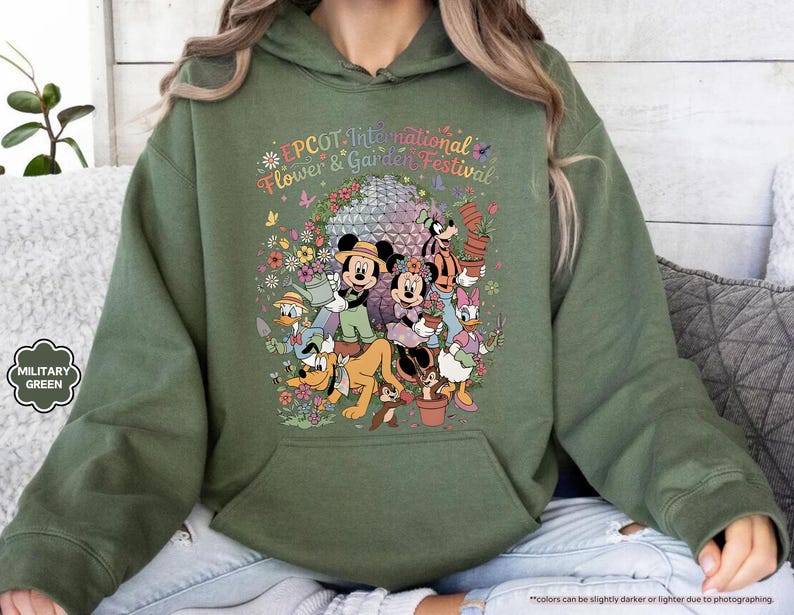 May include: Military green hoodie featuring a colorful graphic of Disney characters at the EPCOT International Flower & Garden Festival. The design includes Mickey and Minnie Mouse, Donald Duck, and Goofy, surrounded by flowers and the festival's logo.