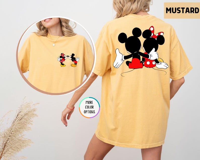May include: Mustard yellow t-shirt with a Mickey and Minnie Mouse graphic. The front shows the characters kissing, and the back features them embracing. The shirt has a relaxed, oversized fit, suitable for casual wear.