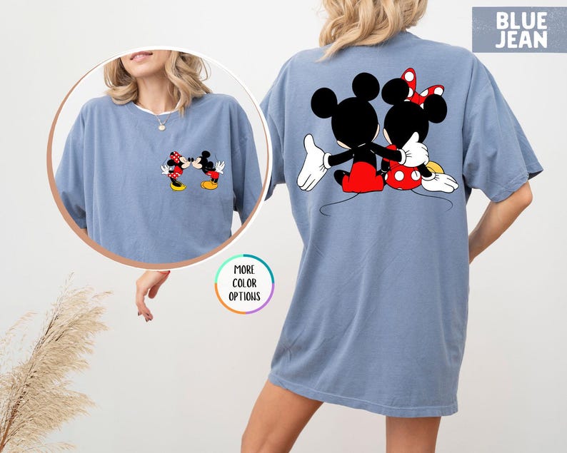May include: Blue jean coloured t-shirt featuring a graphic of Mickey and Minnie Mouse. The front of the shirt shows the characters facing each other, while the back displays them embracing. The shirt has a relaxed fit.