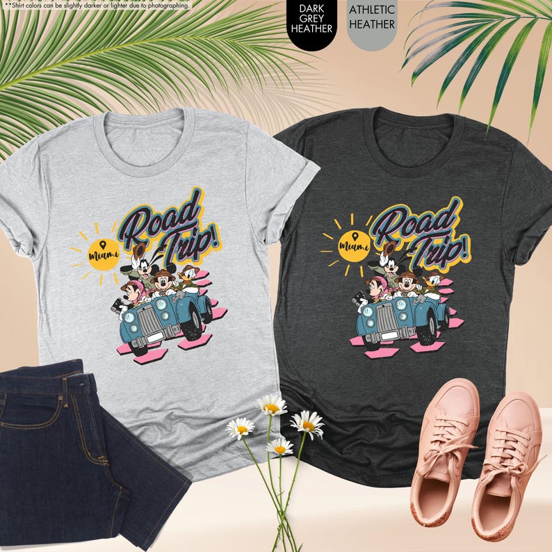 Op de afbeelding: Twee grijze t-shirts met een "Road Trip! Miami"-afbeelding met stripfiguren in een blauwe auto. De shirts worden gecombineerd met een donkerblauwe jeans en roze sneakers. De afbeelding bevat ook witte madeliefjes en palmbladeren.