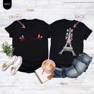 Pu&ograve; includere: T-shirt nere con disegni fronte-retro. Il davanti presenta Topolino e Minnie Mouse con la scritta "Parigi" e la Torre Eiffel in rosso. Il retro mostra la Torre Eiffel con vari personaggi dei cartoni animati.