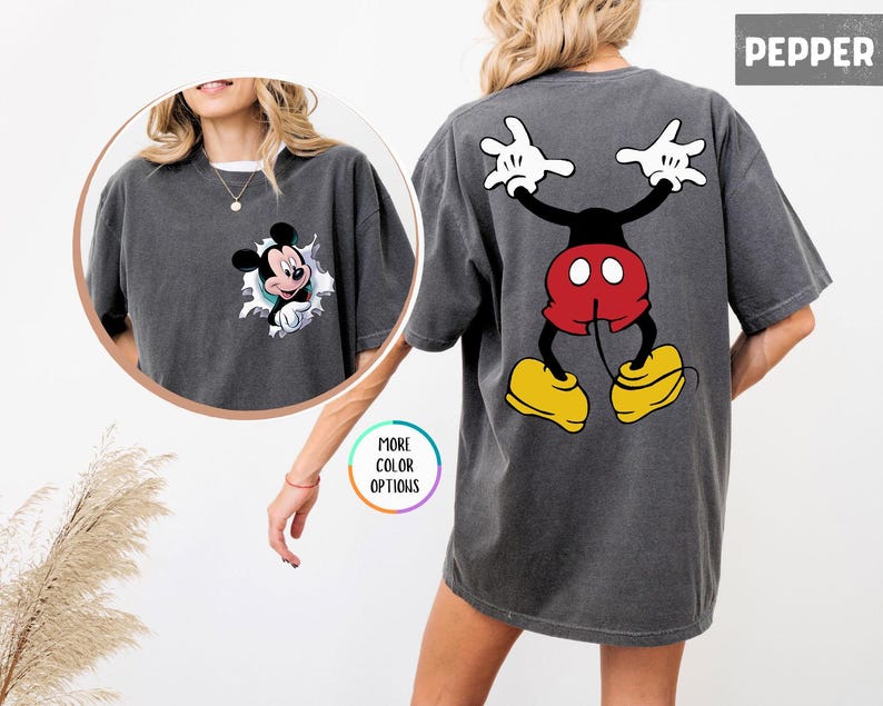 May include: Dark grey t-shirt featuring Mickey Mouse. The front has a circular graphic of Mickey bursting through a torn design. The back displays a large Mickey Mouse graphic with white gloves, red shorts, and yellow shoes. The word "PEPPER" is in the upper right corner.