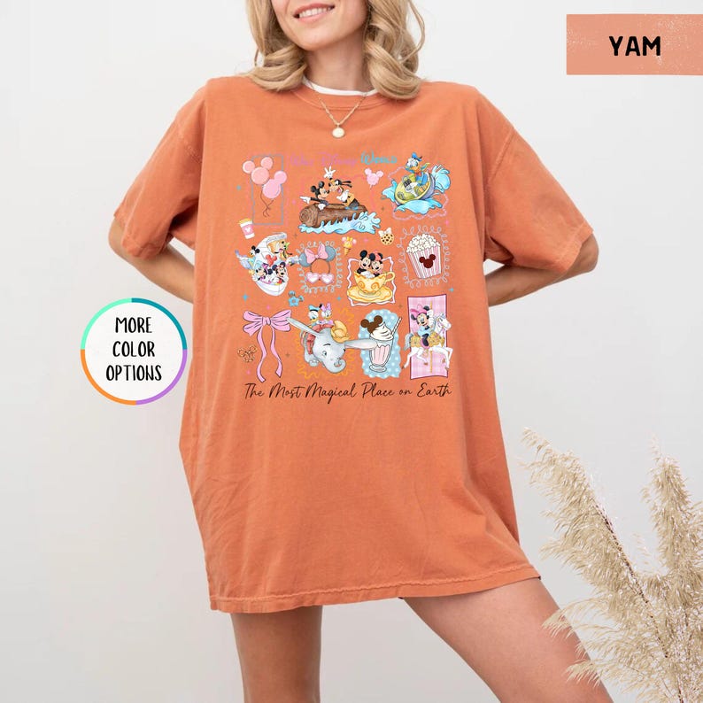 May include: A yam-colored t-shirt featuring a colorful graphic of cartoon characters and the text "The Most Magical Place on Earth." The design includes various characters and icons. The shirt has short sleeves and a relaxed fit.