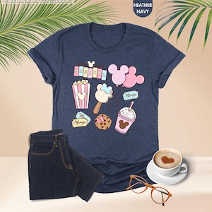 Puede incluir: Una camiseta azul marino jaspeada con un gr&aacute;fico de bocadillos con tem&aacute;tica de Mickey Mouse y el texto "Be Magical".