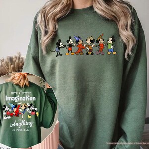 Puede incluir: Sudadera verde militar con una fila de personajes de dibujos animados en el pecho. La parte trasera de la sudadera muestra el texto "WITH A LITTLE IMAGINATION ANYTHING IS POSSIBLE" con un gr&aacute;fico de dibujos animados a juego. La sudadera es de color s&oacute;lido.