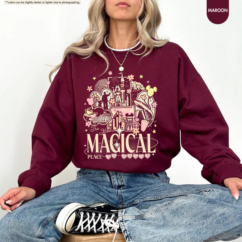 Pode incluir: Camisola bord&ocirc; com um design gr&aacute;fico com um castelo, Mickey Mouse e o texto "The Magical Place". O design inclui estrelas e elementos florais. A camisola &eacute; de cor bord&ocirc; lisa.