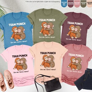 Puede incluir: Una colecci&oacute;n de camisetas en varios colores, incluyendo turquesa, oliva y rosa. Cada camiseta presenta el texto "TEAM PUNCH" sobre una ilustraci&oacute;n de dos monos abraz&aacute;ndose, con la frase "You are never alone!" debajo.