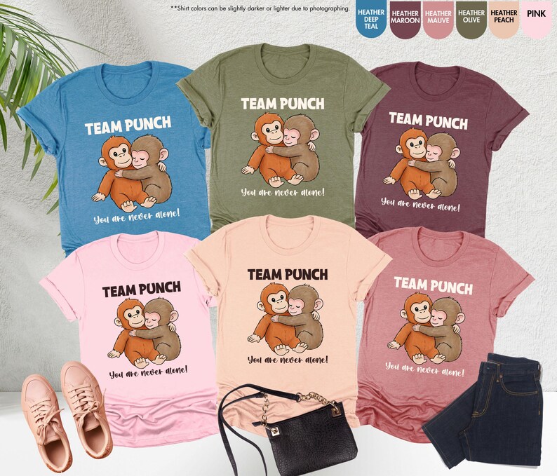 Puede incluir: Una colecci&oacute;n de camisetas en varios colores, incluyendo turquesa, oliva y rosa. Cada camiseta presenta el texto "TEAM PUNCH" sobre una ilustraci&oacute;n de dos monos abraz&aacute;ndose, con la frase "You are never alone!" debajo.