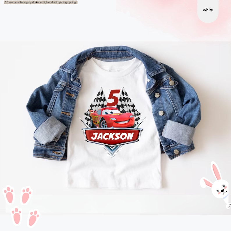 Op de afbeelding: Wit T-shirt met een rode raceauto-afbeelding, geblokte vlaggen en het nummer 5. De tekst "JACKSON" staat onder de auto.