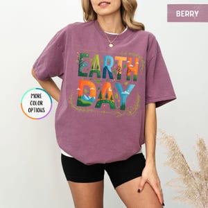 May include: A purple t-shirt with the words "Earth Day" in colorful letters with a nature-themed design. The letters are surrounded by a leafy border.