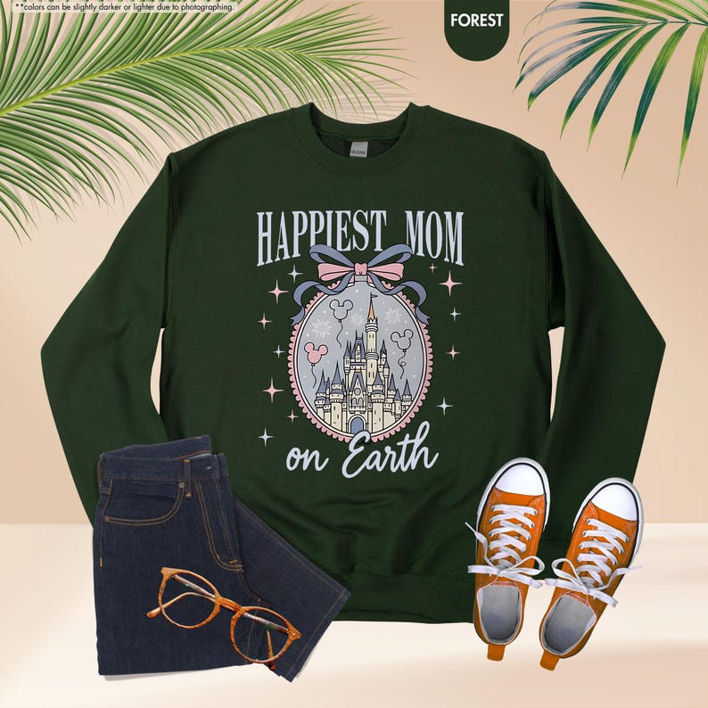 May include: A forest green sweatshirt with the text "HAPPIEST MOM on Earth" above a castle illustration. The image includes a pair of blue jeans, orange sneakers, and eyeglasses.