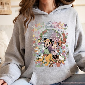 May include: Sport grey hoodie featuring a colorful graphic of Disney characters, including Mickey and Minnie Mouse, surrounded by flowers and the text "EPCOT International Flower & Garden Festival."
